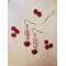 Light Pink Beaded Dangle Earrings with Small Red Heart Charm lays on a table surrounded by red beads. Gold plated fish hook ear wires. 